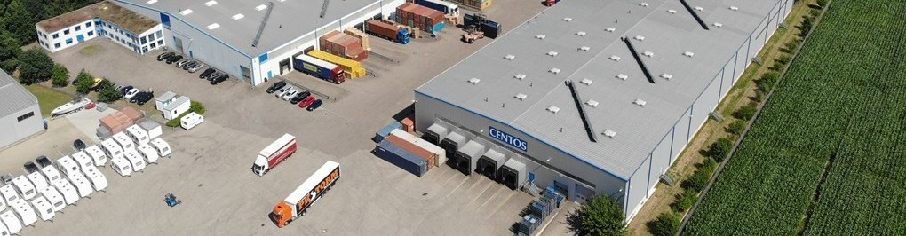 Bild mit einem Menschen, der einen Hubwagen mit einem Karton durch eine Lagerhalle schiebt